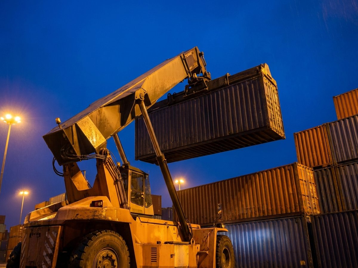 Reach stacker levantando un contenedor marítimo en patio portuario