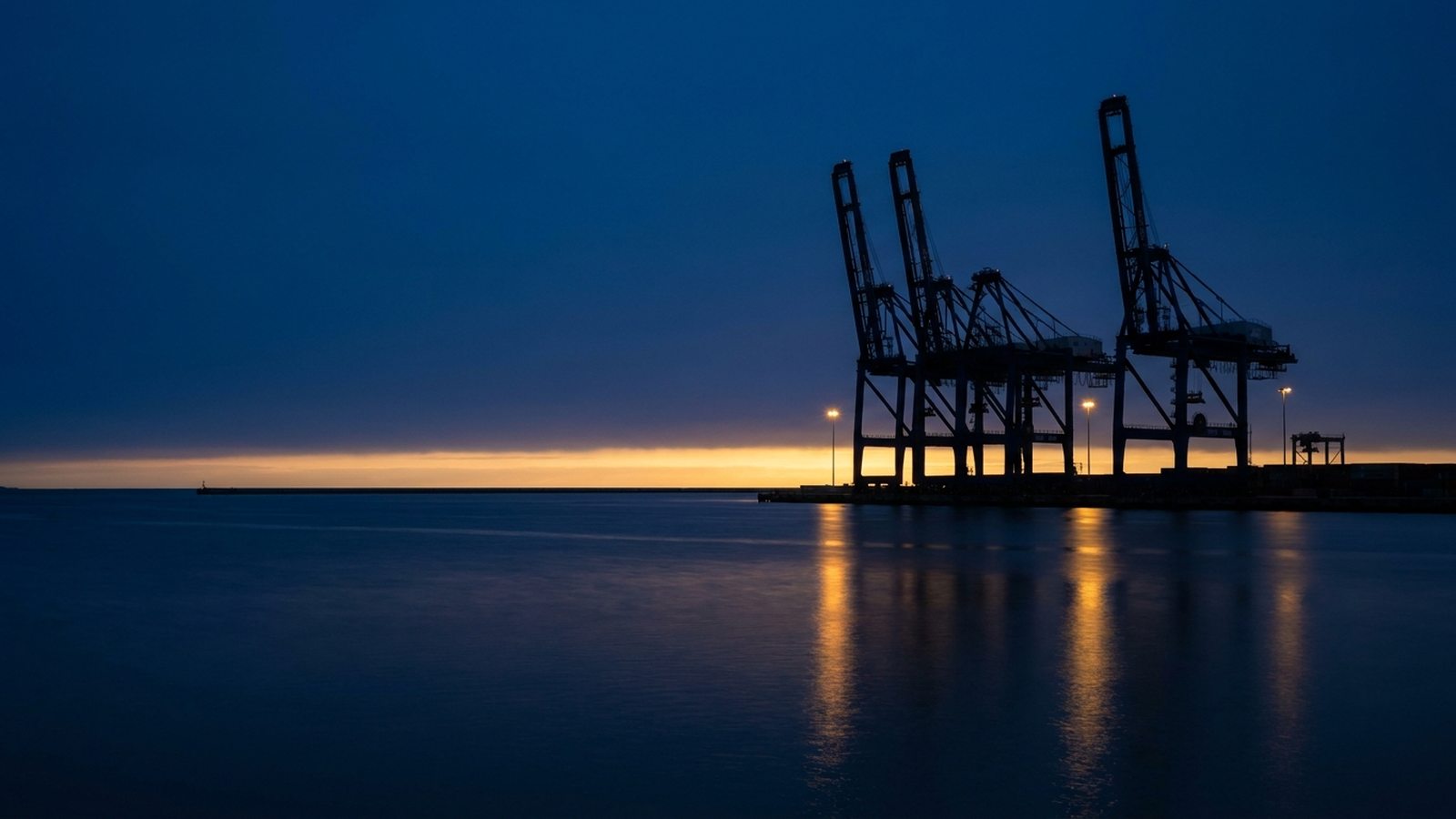 Siluetas minimalistas de grúas portuarias contra el cielo del atardecer